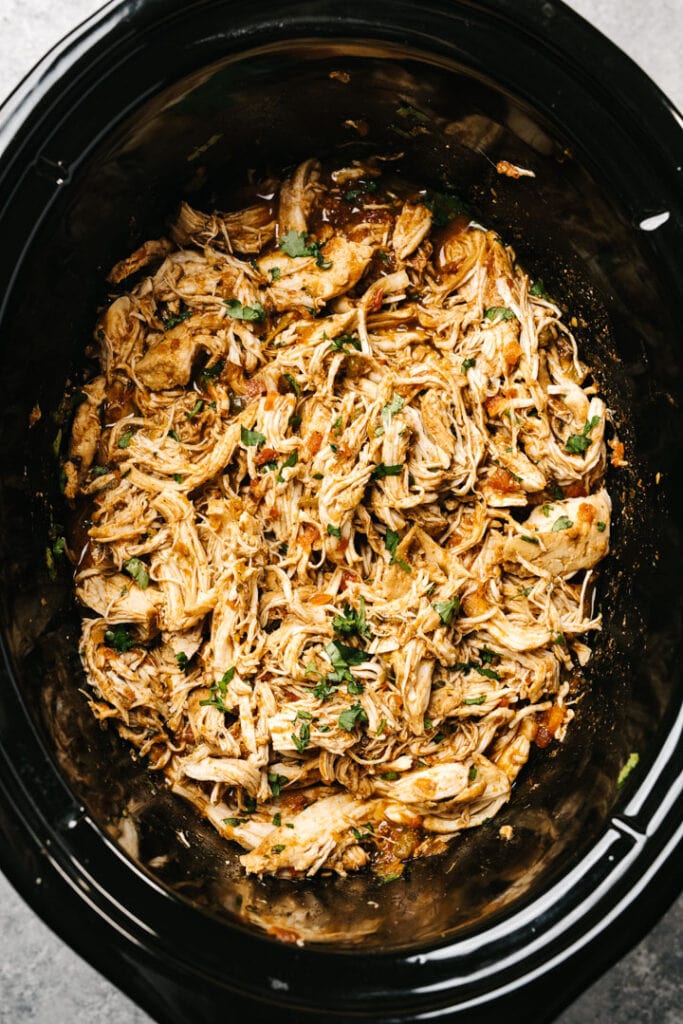 Shredded salsa chicken in a crockpot tossed with cilantro and cooking liquids.