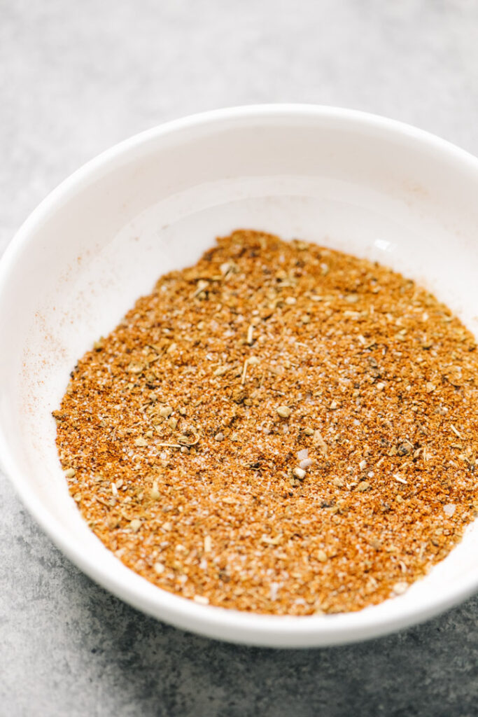 Fajita spices mixed in a small white bowl on a concrete background.
