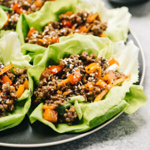 Side view, ground beef lettuce wraps on a black plate, garnished with sesame seeds.