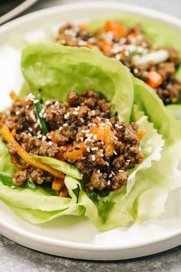 Side view, two ground beef lettuce wraps on a white plate, garnished with sesame seeds.