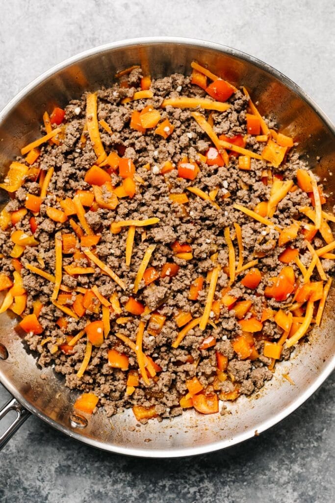 Ground beef with diced red peppers and shredded carrots in a skillet.