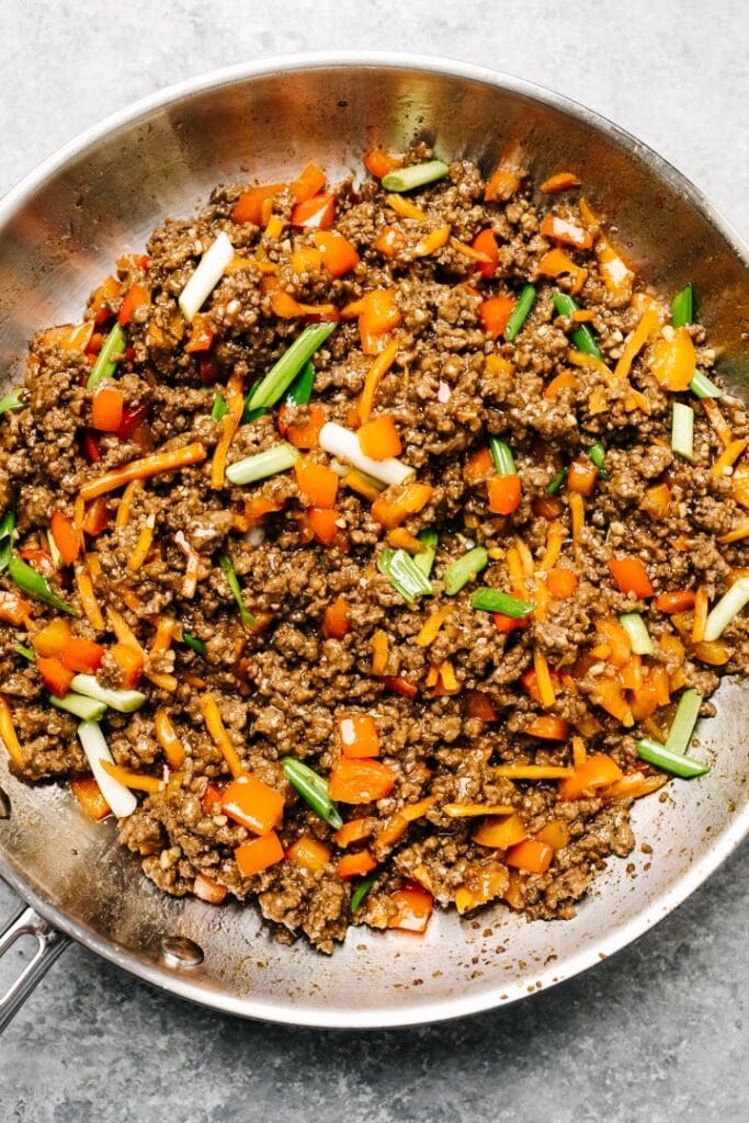 Ground beef lettuce wrap filling in a skillet, with red bell peppers, shredded carrots, and green onions.
