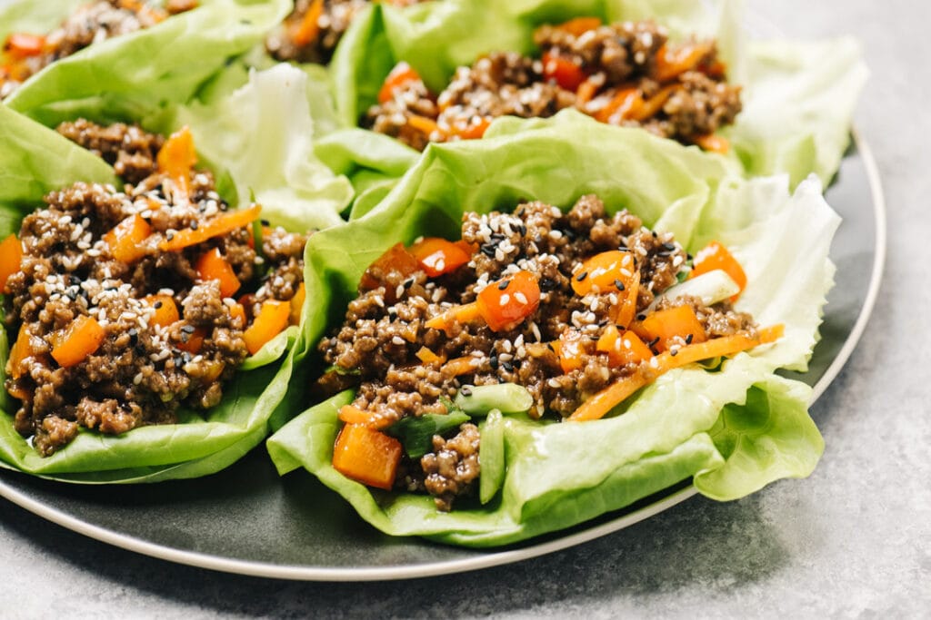 Side view, ground beef lettuce wraps on a black plate, garnished with sesame seeds.