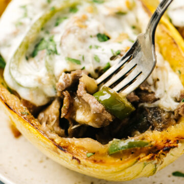 A fork digging into a stuffed spaghetti squash, filled with cheesesteak filling and topped with provolone cheese.