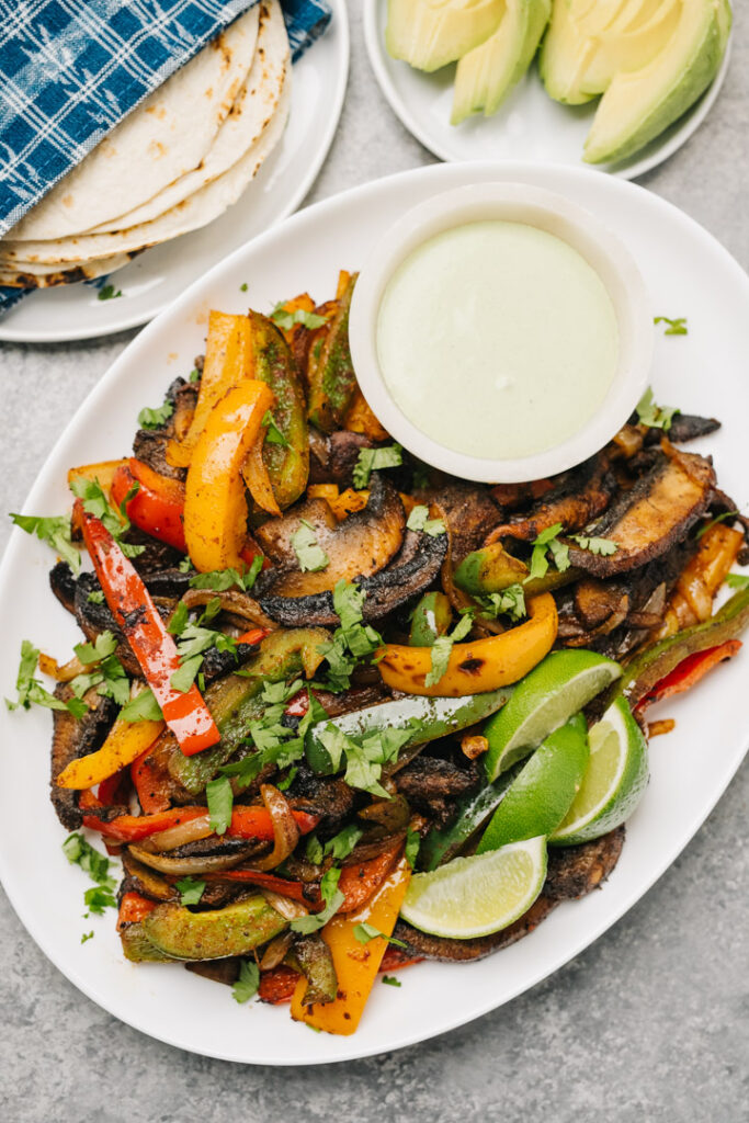 Vegetarian fajita filling on a white platter - sauteed portobello mushrooms, onions, and bell peppers - garnished with lime wedges,