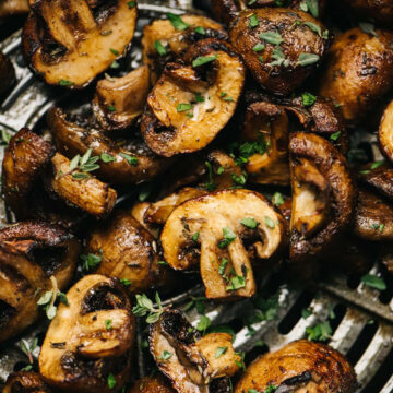 Golden brown air fried mushrooms in the basket of an air fryer, garnished with fresh herbs.