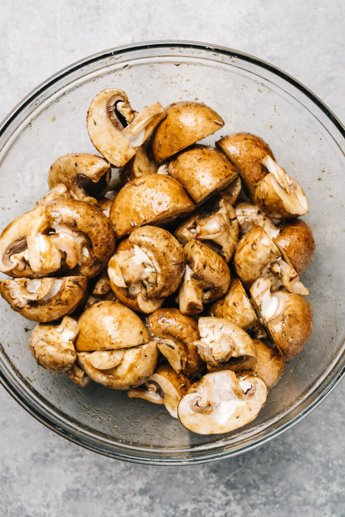 Quartered mushrooms tossed with marinade in a glass mixing bowl.