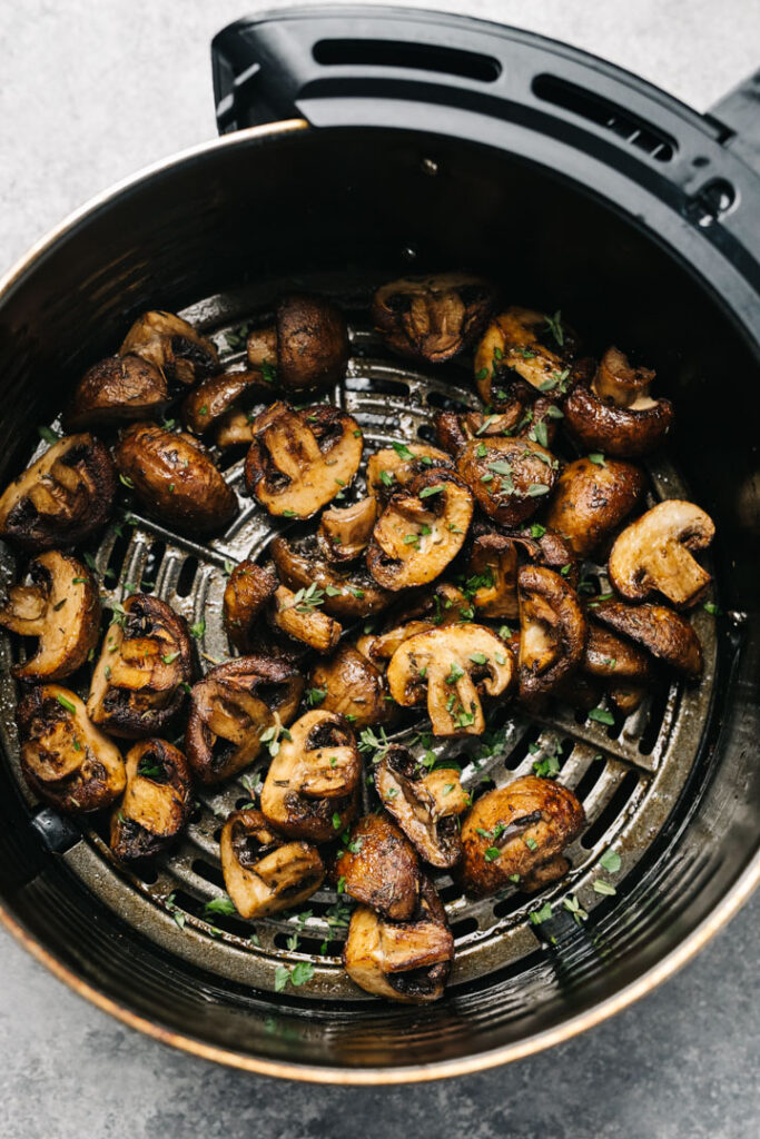 Golden brown air fried mushrooms in the basket of an air fryer, garnished with fresh herbs.