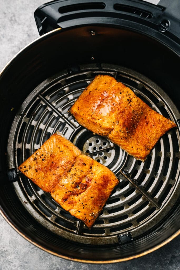 Two cooked salmon fillets in an air fryer basket.