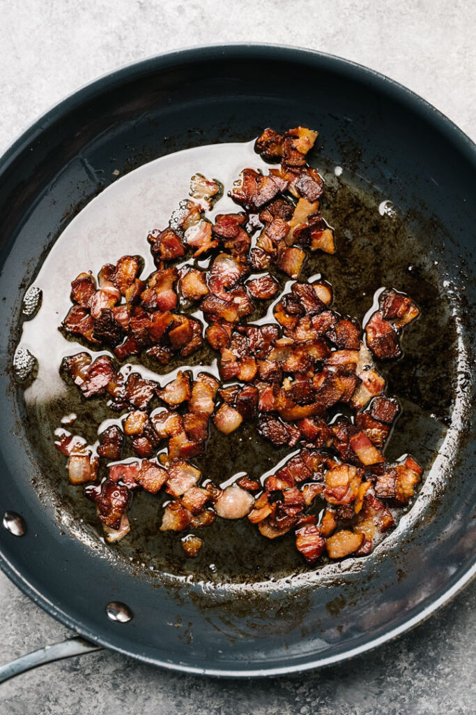 Sauteed chopped bacon in a dark grey skillet.