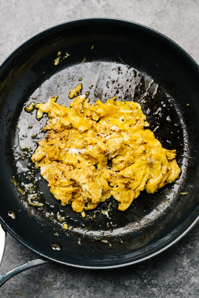 Eggs scrambled in rendered bacon fat in a dark grey skillet.
