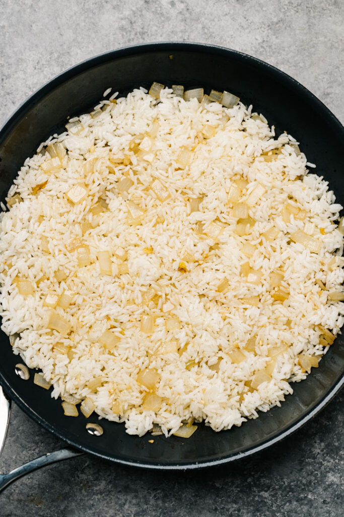 Day old white rice frying in a skillet with onions and garlic.
