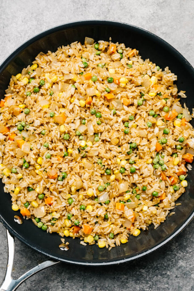 Fried rice in a skillet with onions, peas, carrots, and corn.