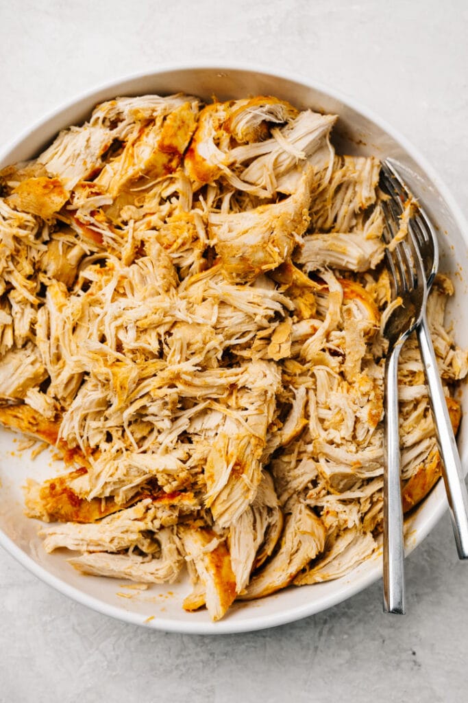 Shredded buffalo chicken in a white bowl with two forks.