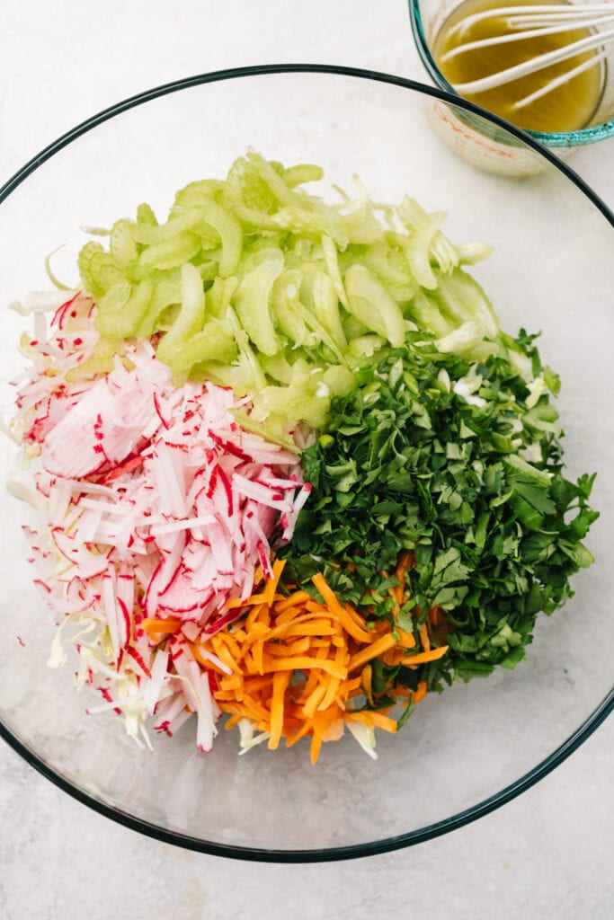 Shredded cabbage, carrots, celery, and radishes in a bowl with chopped parsley.