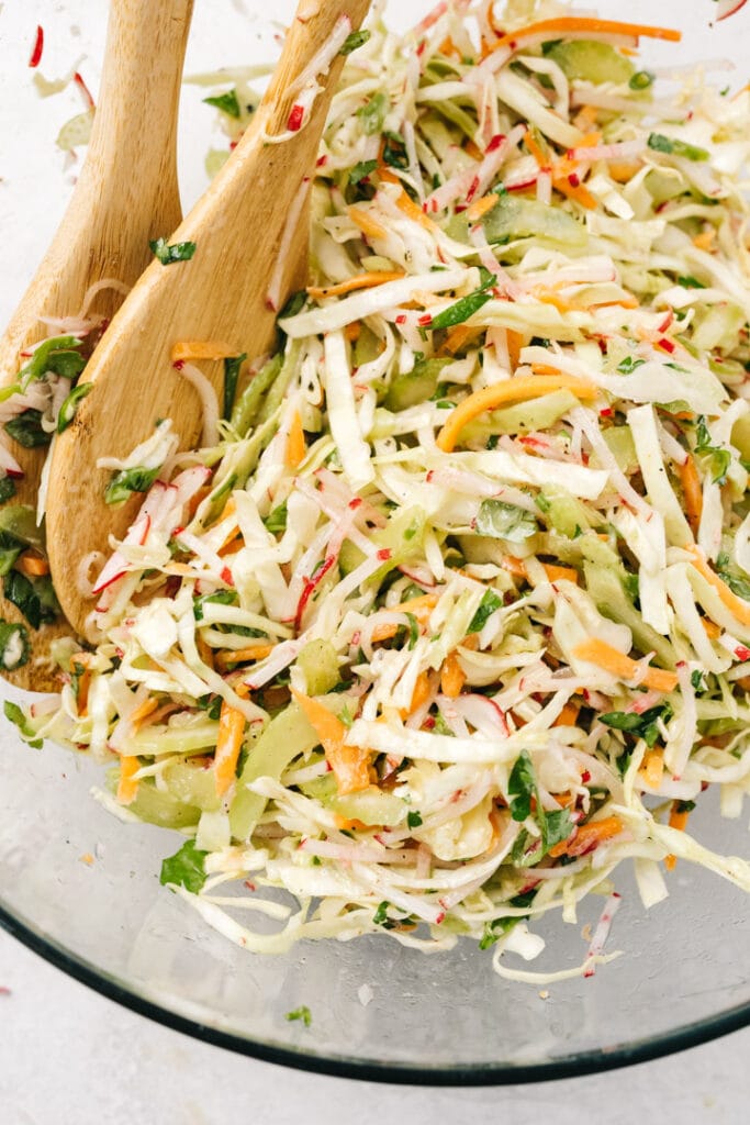 Tangy vinegar coleslaw in a glass mixing bowl with wood serving utensils.