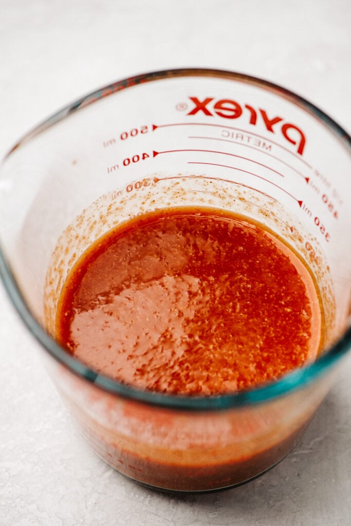 Two hot sauces mixed with seasonings in a glass pyrex mixing cup.