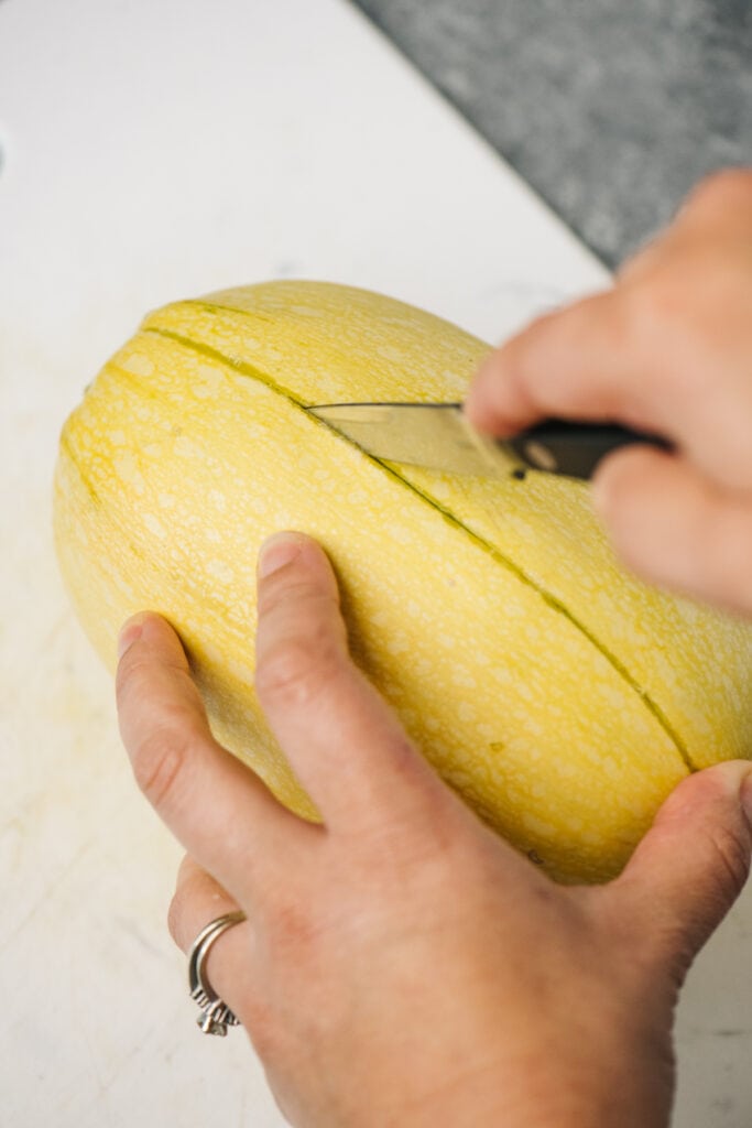 From the side, making cuts into a spaghetti squash using a paring knife to safely cut in half.