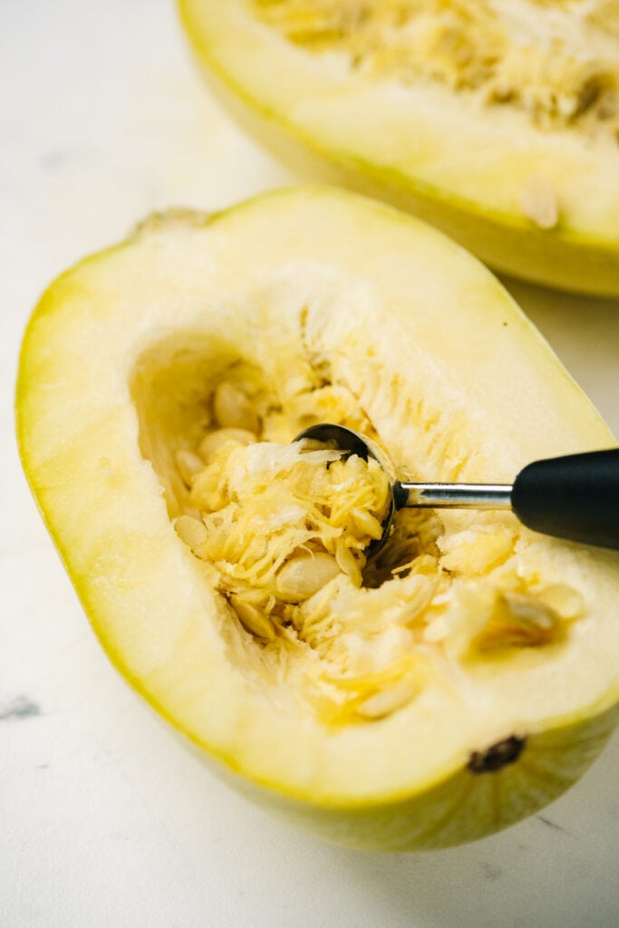 Side view, removing the seeds and membranes from a spaghetti squash using a melon baller.