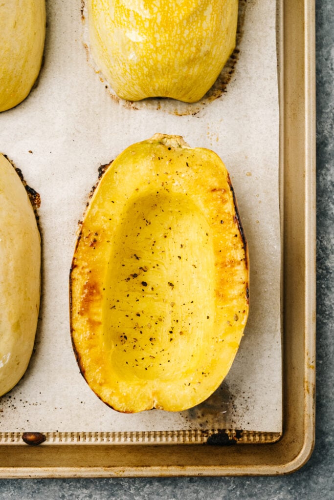 Roasted spaghetti squash halves on a parchment lined baking sheet.