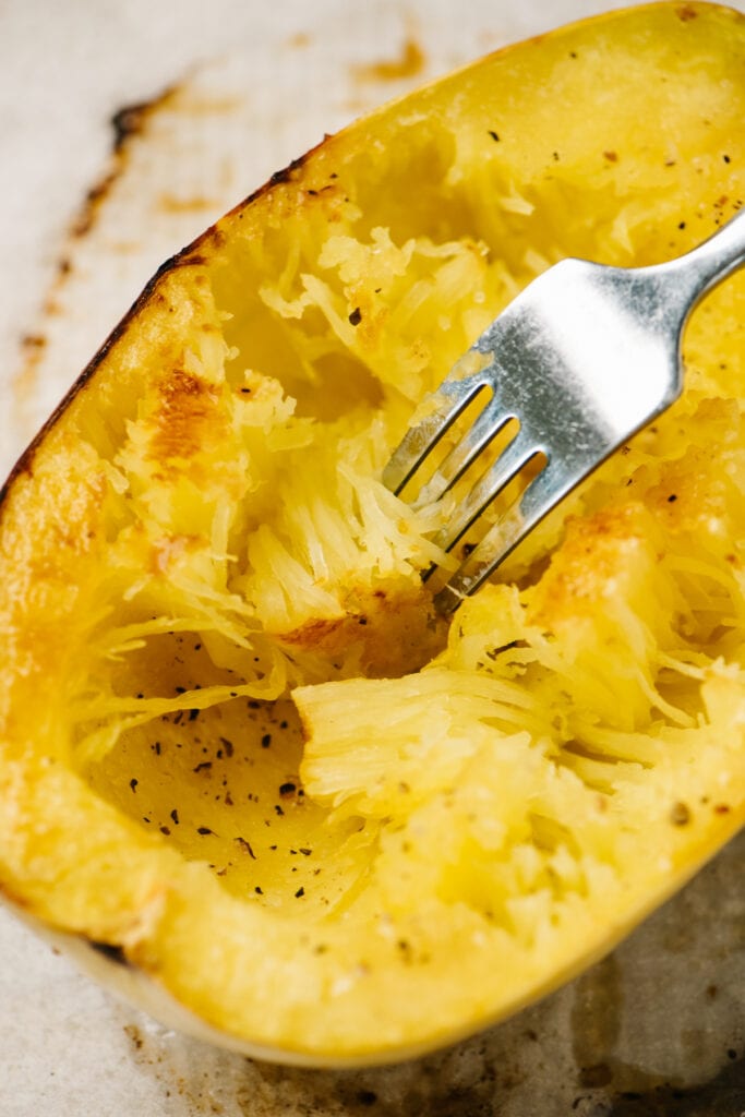 Side view, a fork gently raking the flesh from a roasted spaghetti squash.