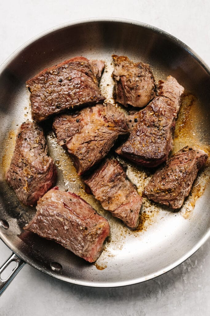 Chuck roast pieces searing in a skillet.