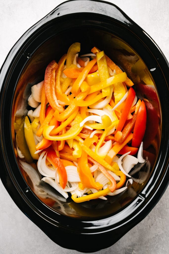 Thinly sliced onions and peppers in a slow cooker.