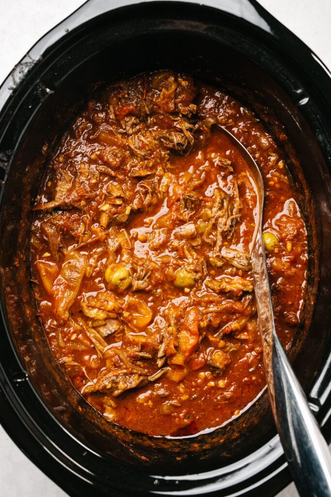 Ropa vieja in a slow cooker with a silver serving spoon.