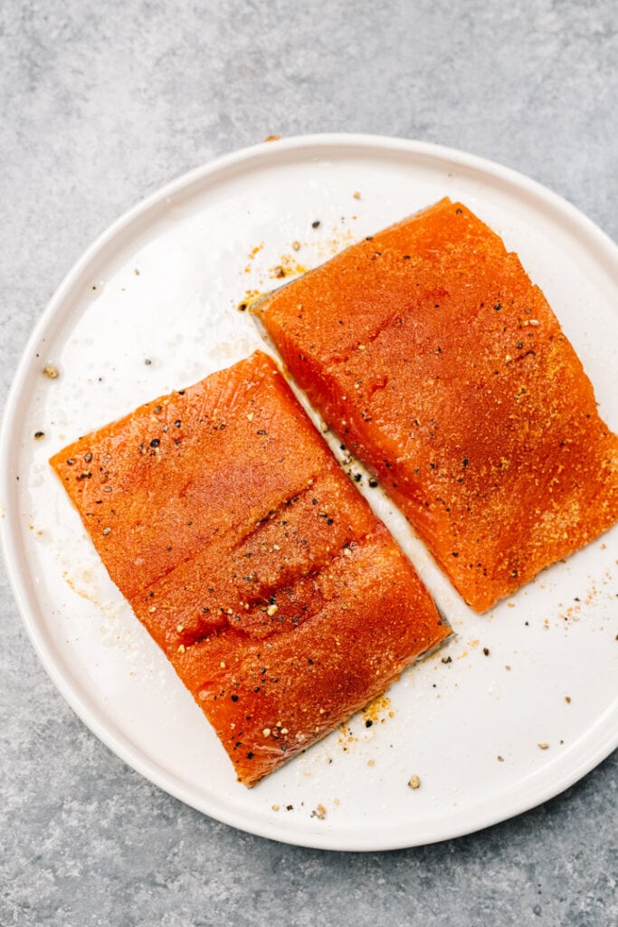 Two salmon fillets rubbed with olive oil and seasoned with salt, pepper, and garlic powder.