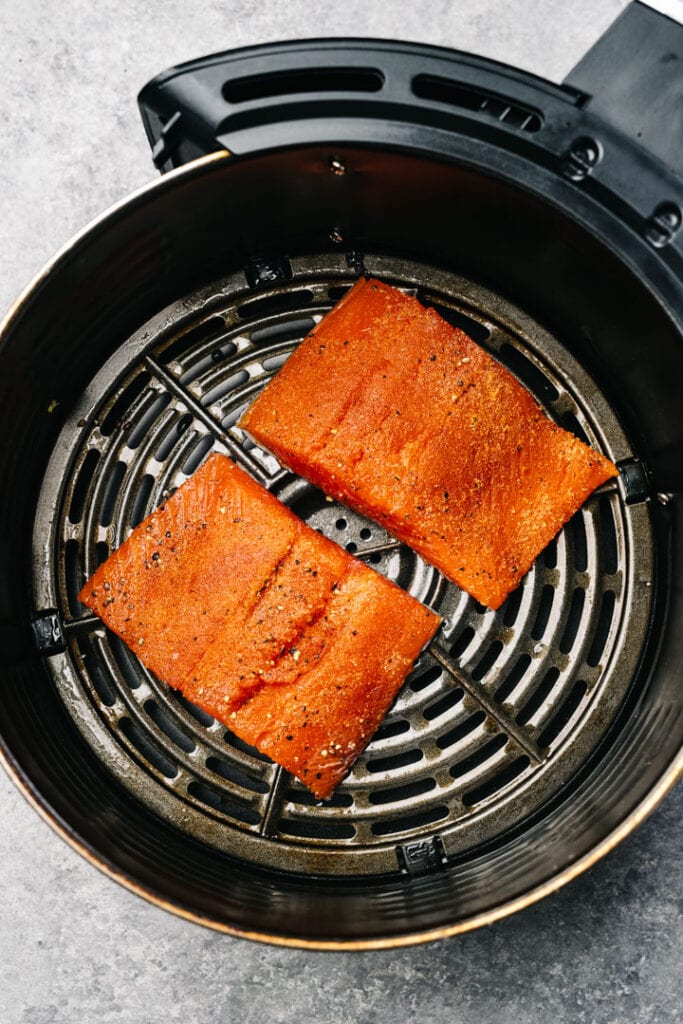 Two seasoned salmon fillets in an air fryer basket.