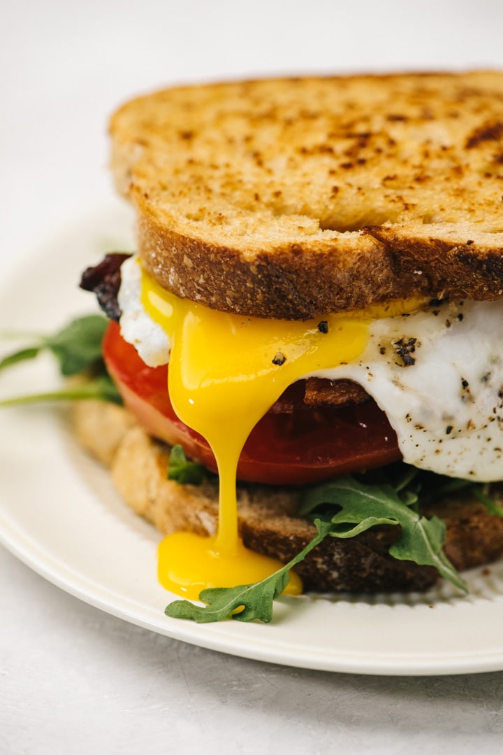 Side view, runny egg yolk running down the side of a BLT breakfast sandwich.