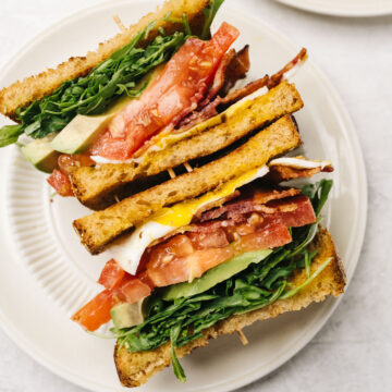 A BLT breakfast sandwich sliced in half and sliced sides up on a white plate, showing the interior.