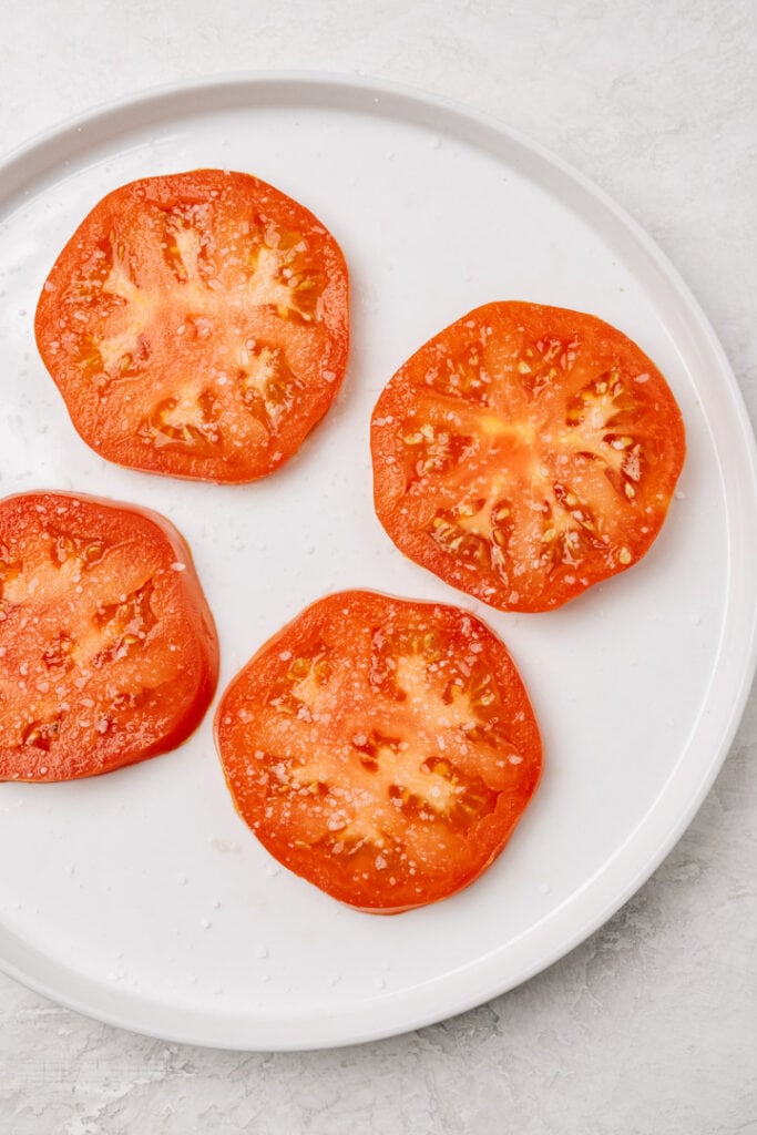 Tomato slices sprinkled with salt on a white plate.