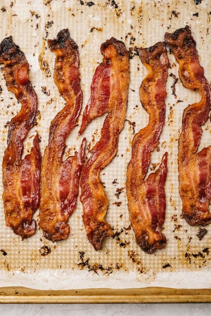 Crispy slices of bacon on a parchment lined baking sheet.