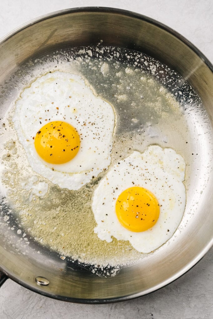 Two fried eggs in a skillet seasoned with ground pepper.