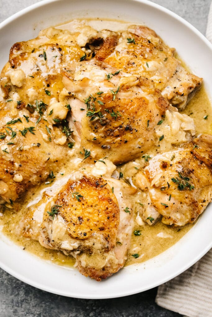 Creamy garlic chicken in a low white serving bowl, with a linen napkin to the side.