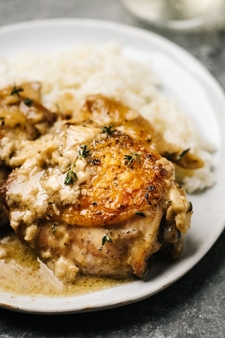 Side view, creamy garlic chicken thighs over rice on a white plate.
