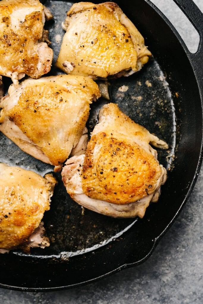 Seared pieces of chicken thighs in a cast iron skillet.