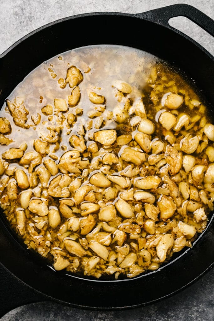 Sautéed whole garlic cloves simmering with white wine in a cast iron skillet.