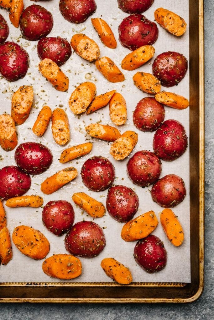 Seasoned potatoes and carrots on a parchment lined baking sheet.