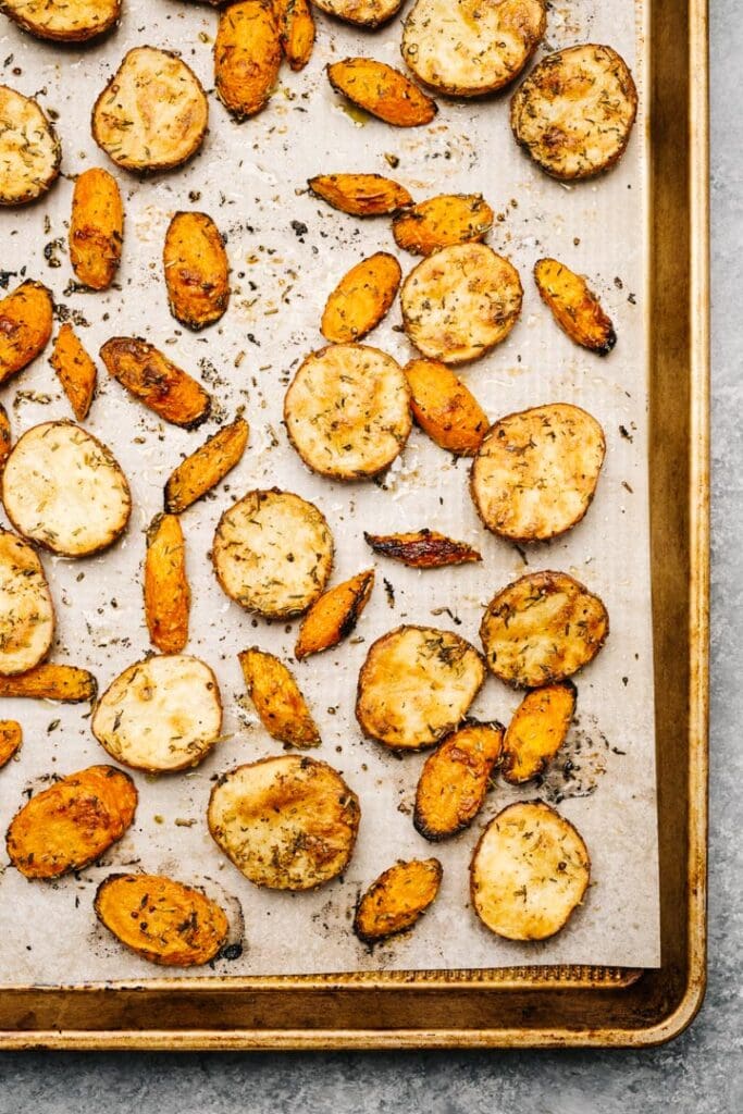 Roasted new potatoes and carrots on a parchment lined baking sheet.