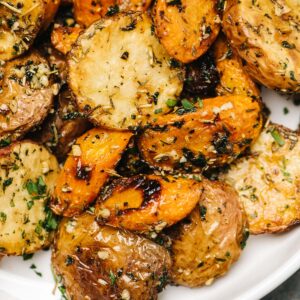 Roasted potatoes and carrots tossed with garlic her butter in a white serving dish.