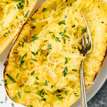 Two roasted spaghetti squash halves on a white plate, garnished with chopped parsley.
