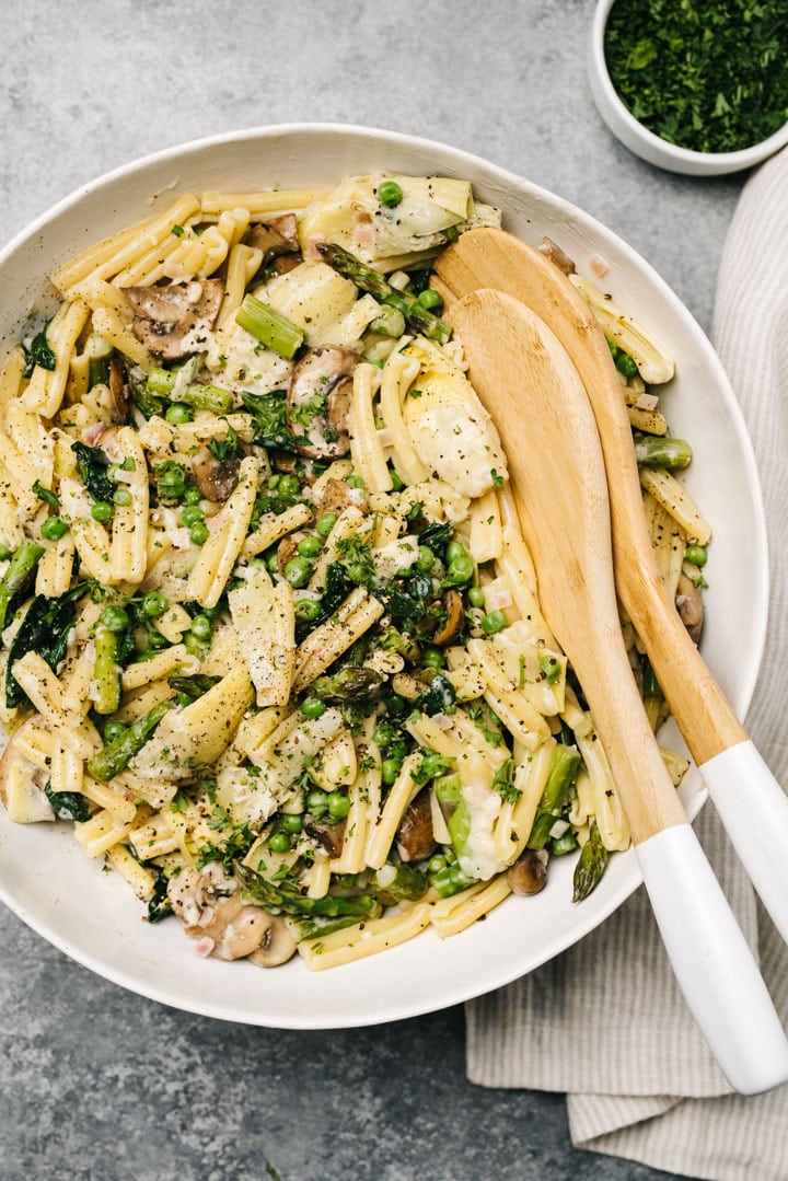 A large bowl of pasta primavera tossed with spring vegetables and garnished with fresh parsley and ground pepper.