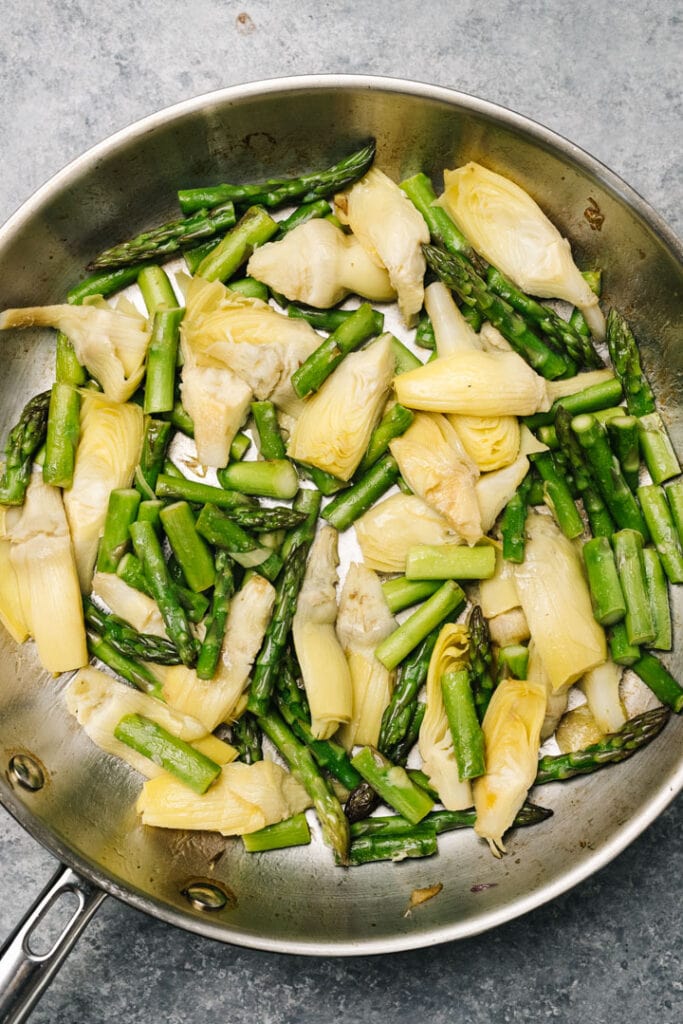 Sauteed pieces of asparagus with canned artichoke hearts in a skillet.
