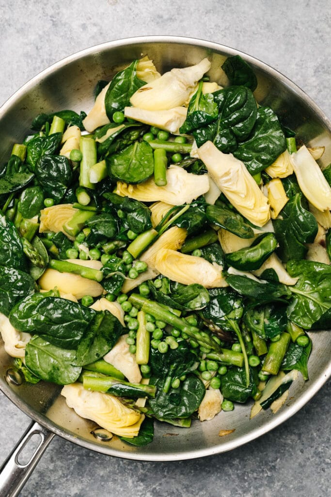 Sauteed asparagus, artichoke hearts, peas, and spinach in a skillet.