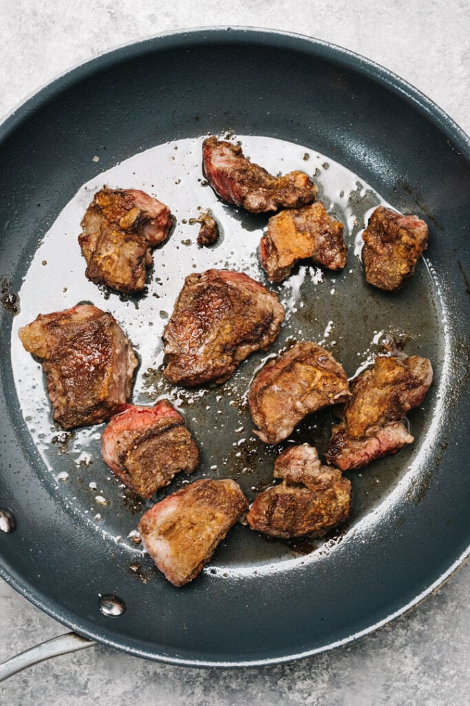 Seared pieces of beef chuck roast in a skillet.