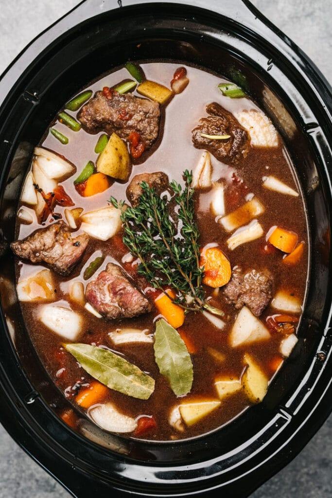 Vegetable beef soup with fresh thyme and bay leaves in a crockpot before slow cooking.