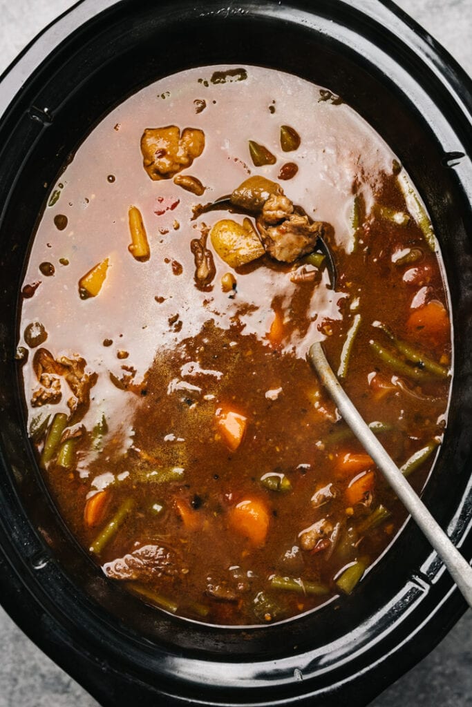A metal ladle tucked into vegetable beef soup into a crockpot.
