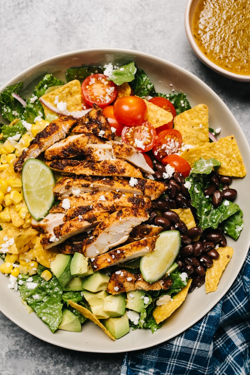 Taco salad with chicken in a low tan salad bowl with corn, black beans, avocado, tomato, and tortilla chips.